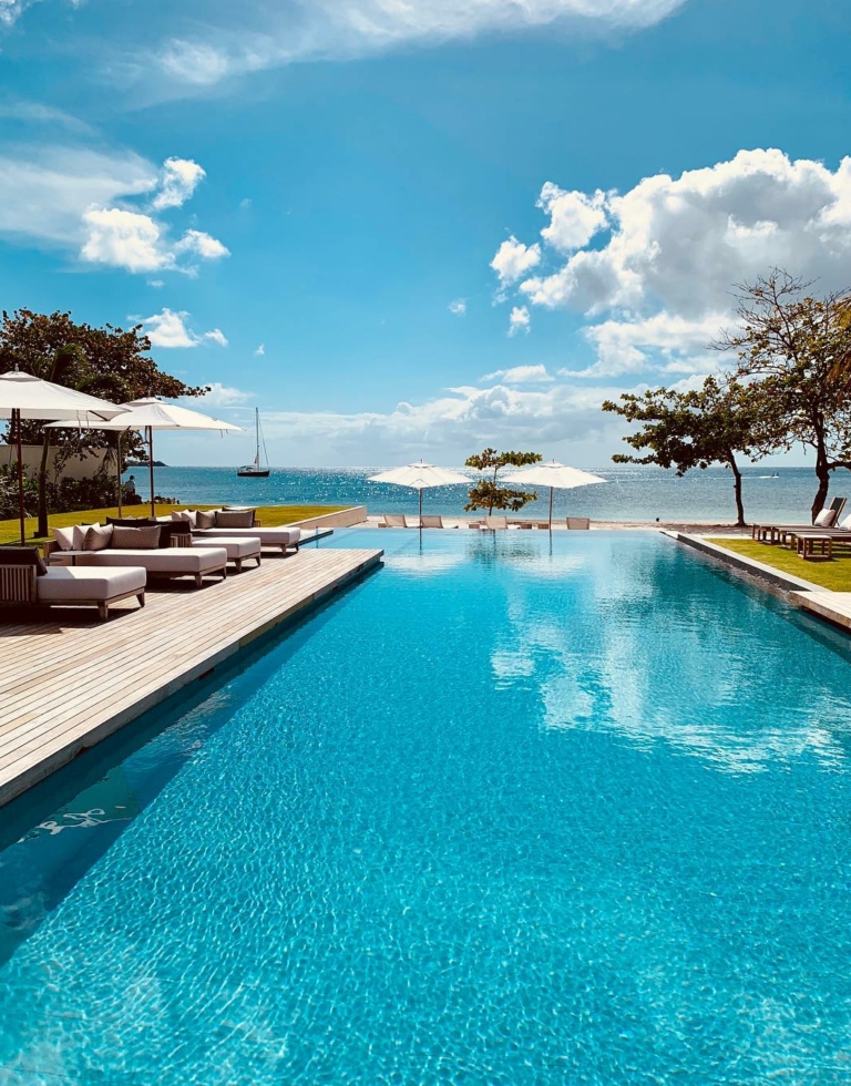 Terrasse softline en teak et ipé entourant grande piscine donnant sur mer avec ciel bleu dégagé